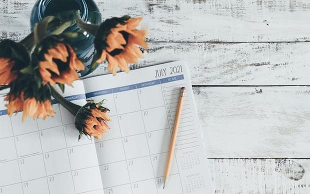 A blank day planner notebook open on a white painted tabletop next to a vase with flowers.